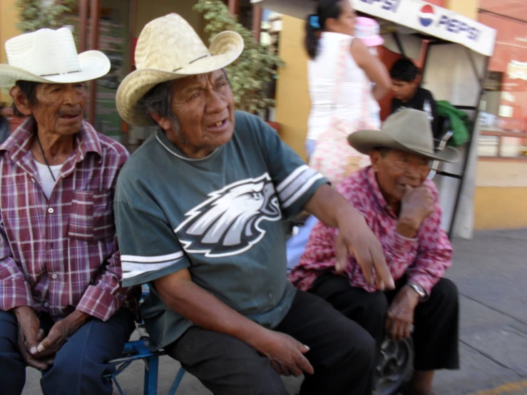 three older men in cowboy hats sit on the street