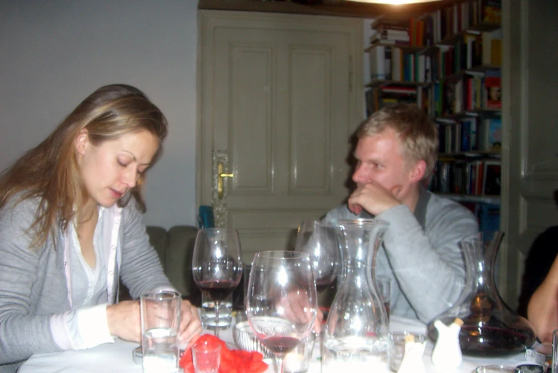 a young man is reading while a woman sits in front of him at a table with several glasses