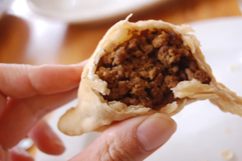 someone holding a dessert covered with meat and bread