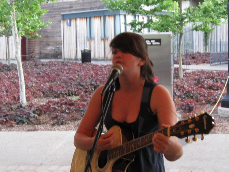 woman singing with guitar next to metal structure