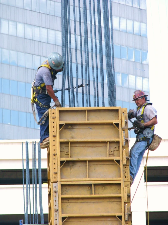 two construction workers standing on top of a yellow truck