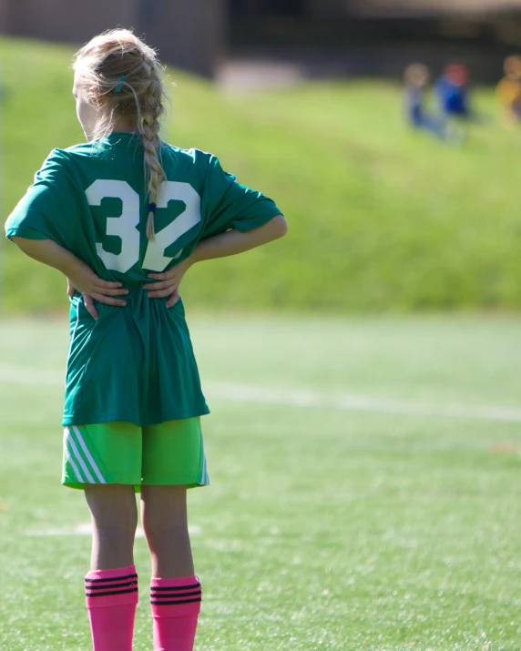 a girl in a jersey and knee socks standing on a soccer field with her hands on her back