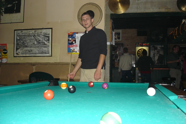 a young man standing by a pool table