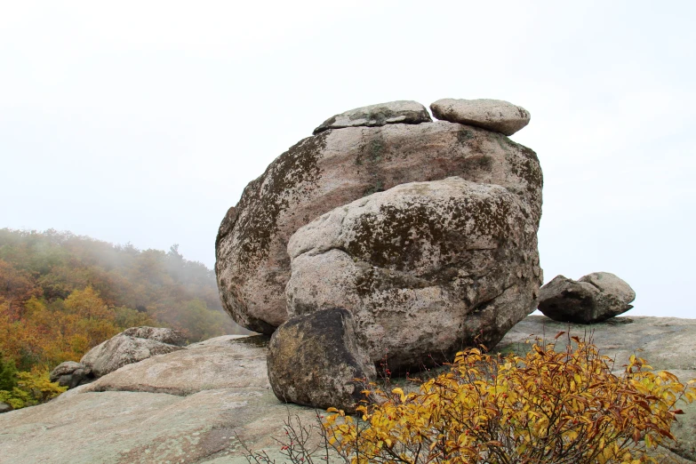 a rock on top of a hill with trees behind it