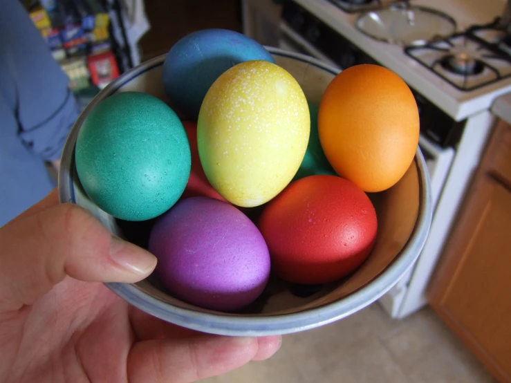 a person holding a bowl with colorful eggs in it