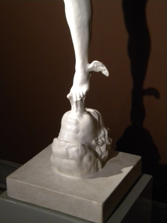 an white sculpture standing on a block with a foot on it