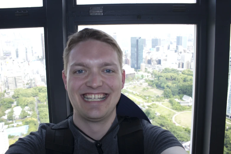 a smiling man taking a selfie with a city skyline in the background