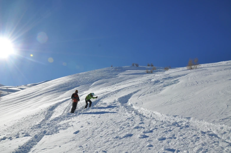 two skiers trekking down a slope with the sun shining