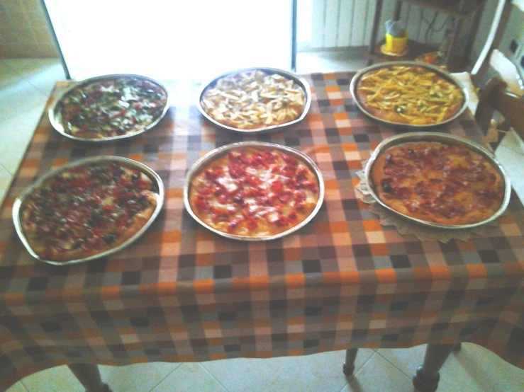 a table with seven pizzas and five other pans