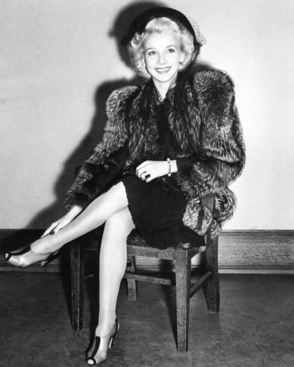 a woman wearing a fur coat is sitting on a chair