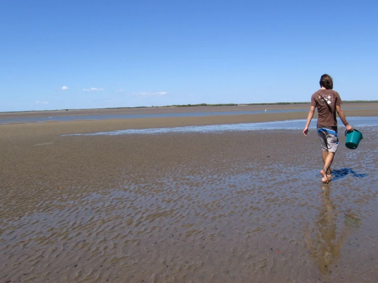 a man walking along the sand holding a bucket