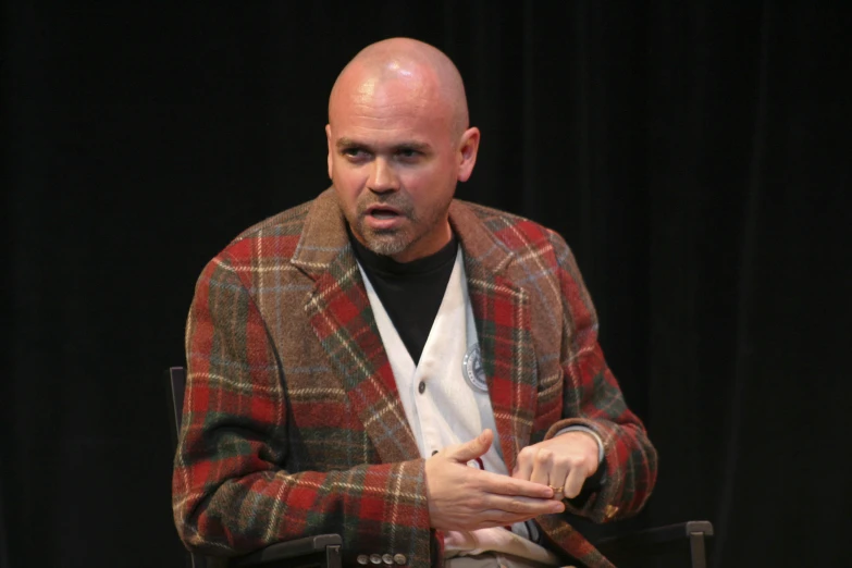 man in red and black coat sitting on chair holding soing