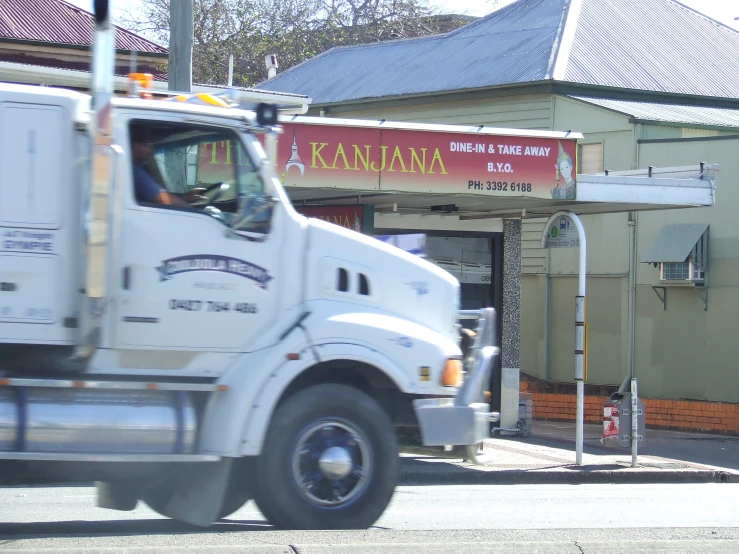 truck traveling down city street near shops and store fronts