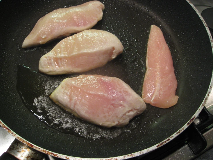 three raw chicken  being fried in a frying pan