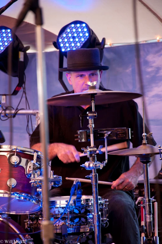 a man with a hat on and lights on his head sitting in front of drums