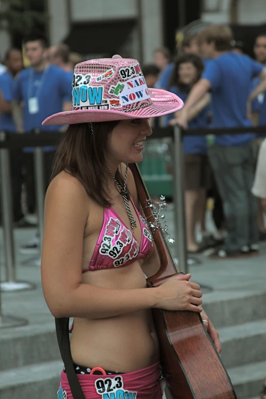 a young woman in a bikini and pink cowboy hat carrying a guitar