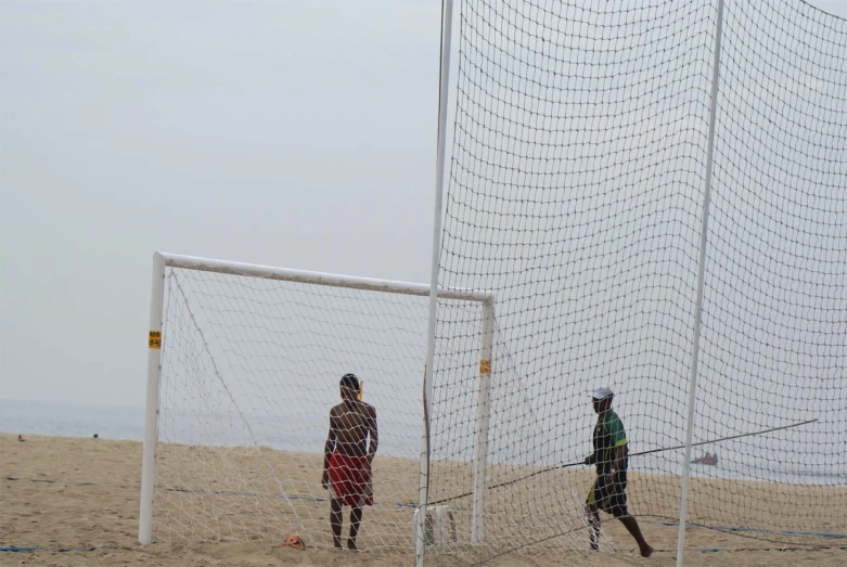 two people playing soccer on the beach near the water