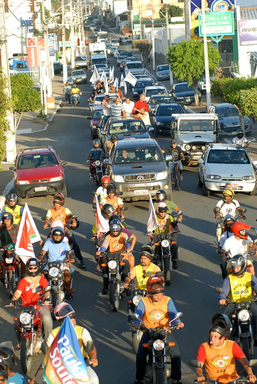 many motorcyclists going through a city area with cars and trucks