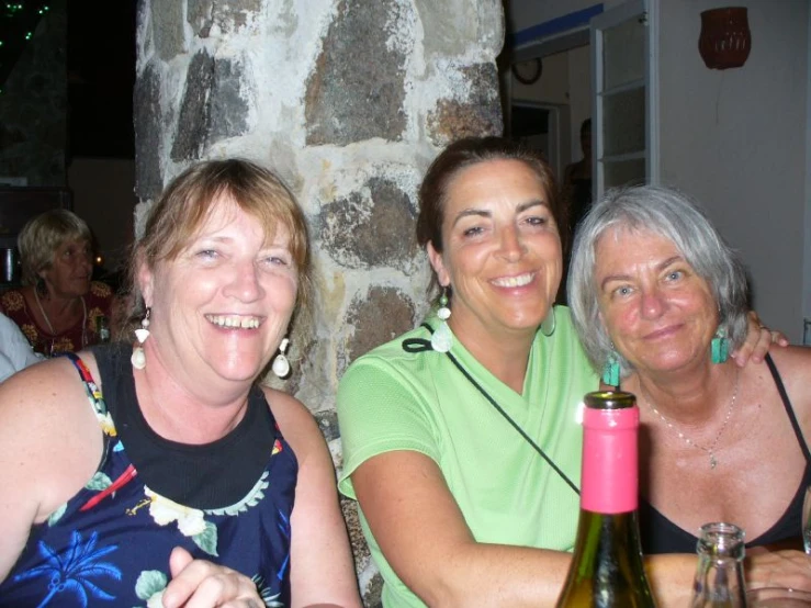 three women sitting at a table with one holding a bottle