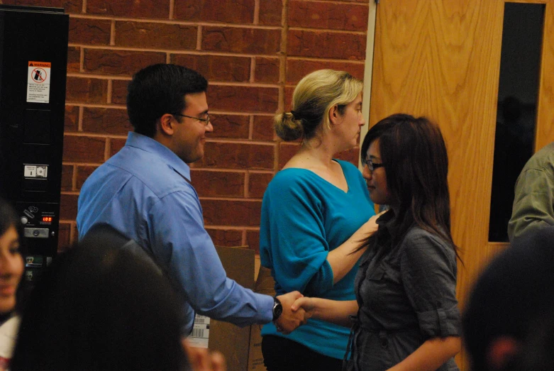 two women shaking hands near a man in a blue shirt