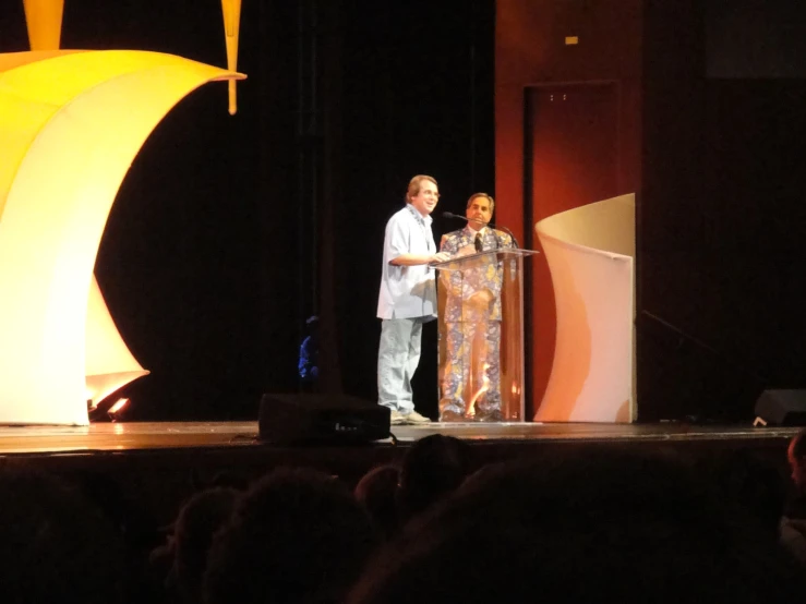 two men standing on stage with microphones behind them