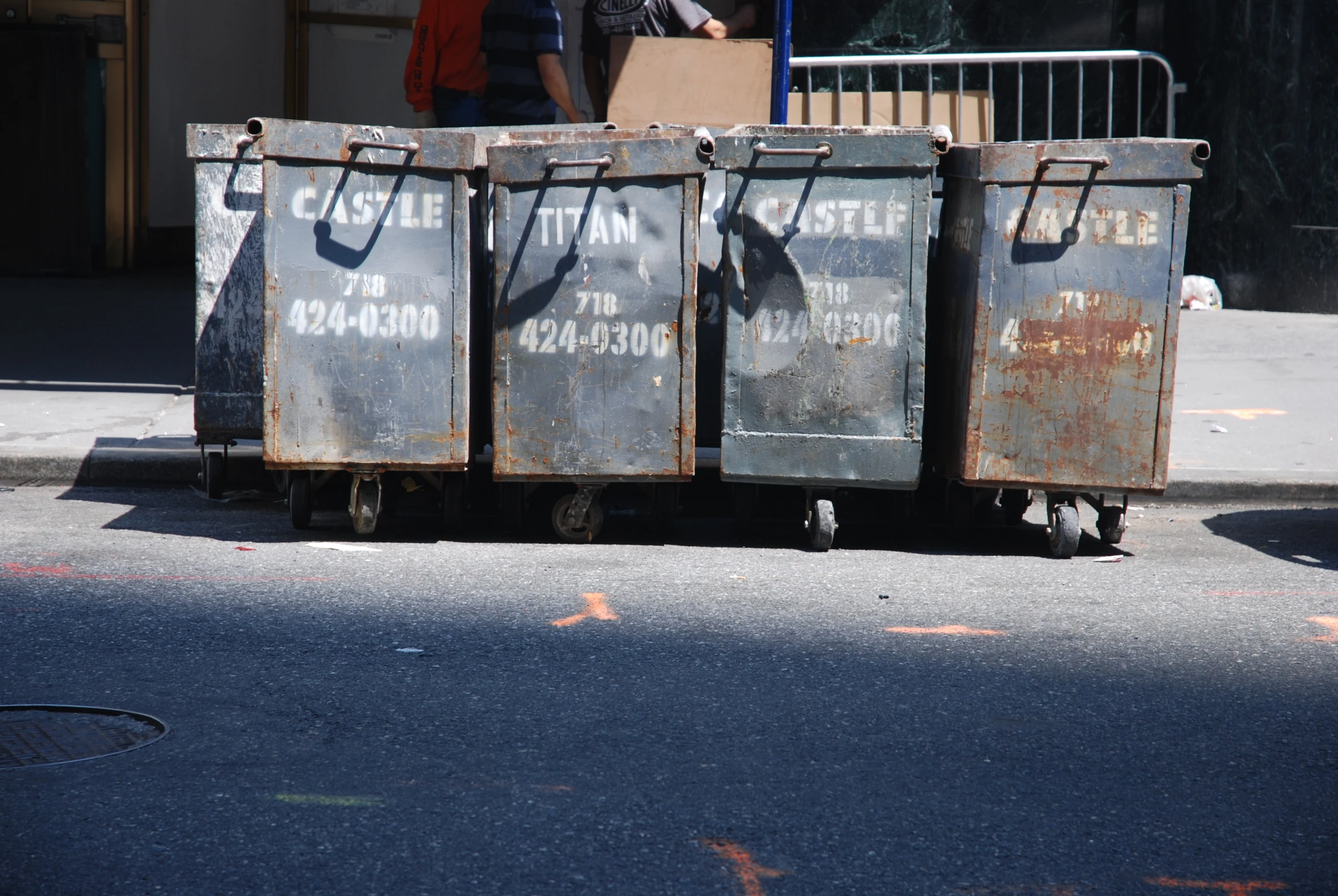 three garbage containers on wheels with people walking around