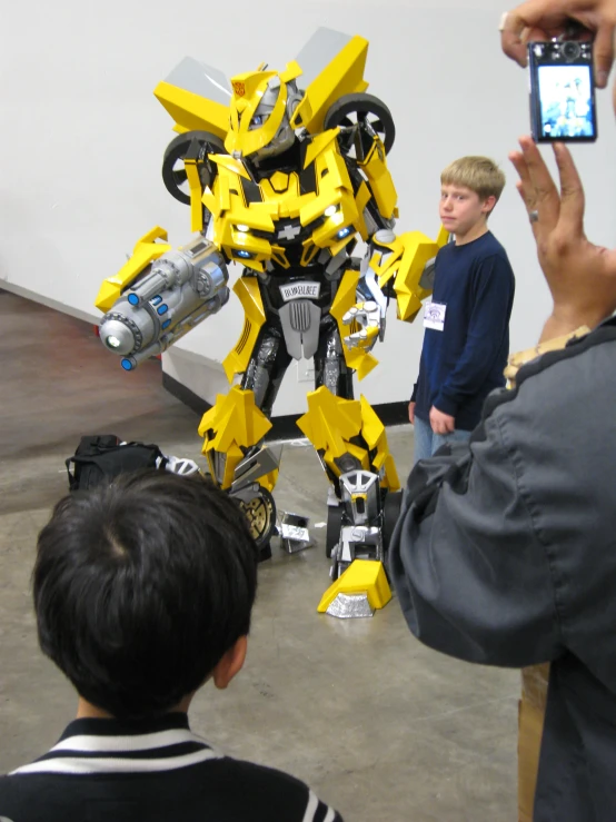 two people holding up phones and two toy robot robots