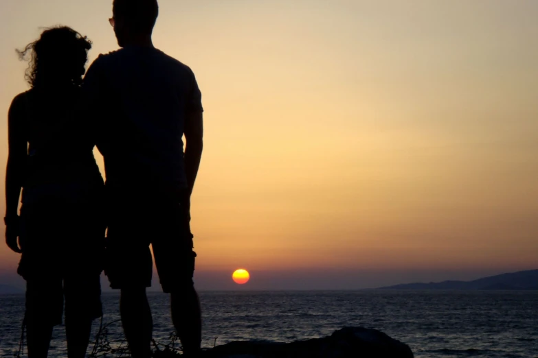 the silhouette of a man and a woman looking out at the ocean