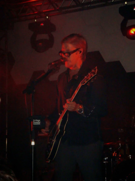 a man with glasses plays a guitar in front of an audience