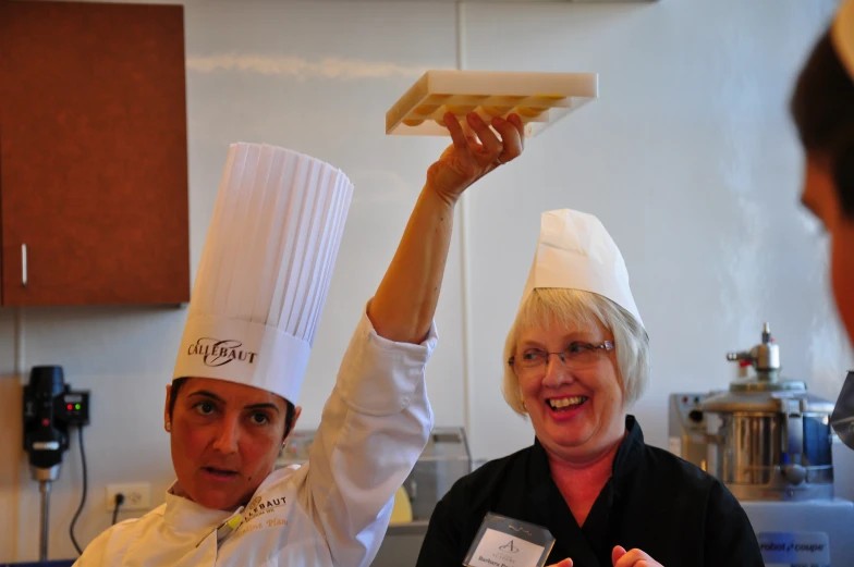 two chefs in white hats and black tops are holding up some doughnut sticks