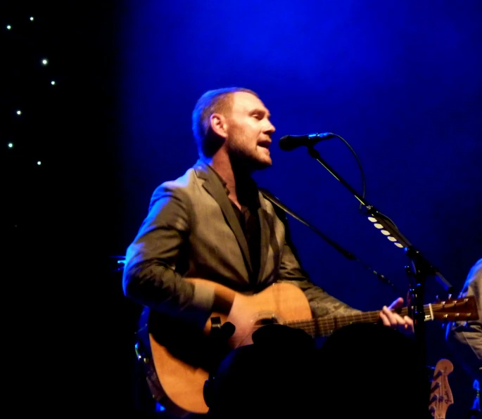 the man is playing a guitar and singing into the microphone