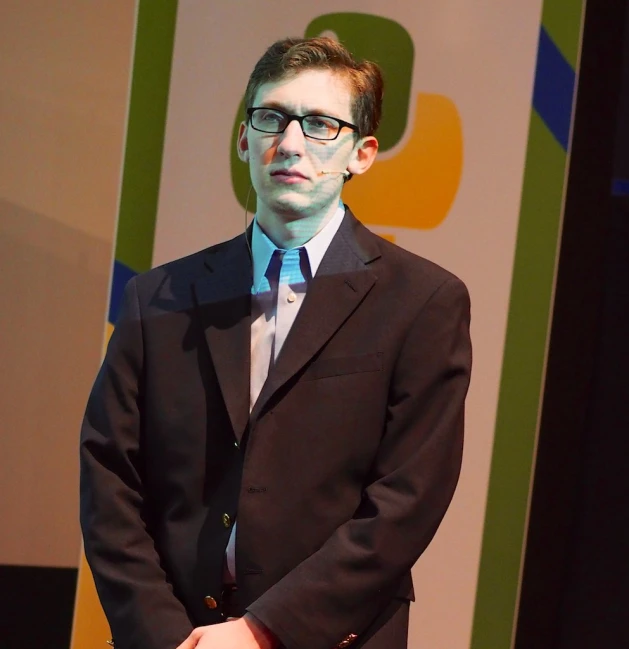 a man standing up at a podium with his hands in his pockets