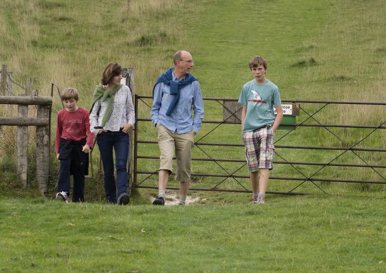 two adults and one child standing near a wooden gate on the grass