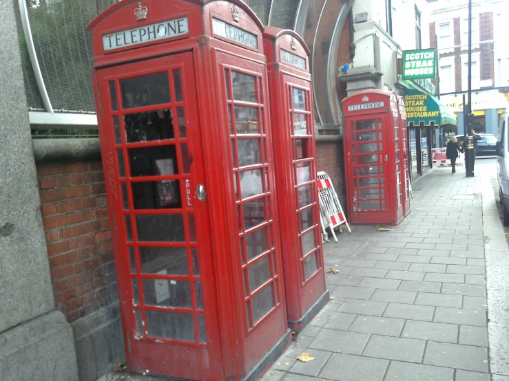 three red telephone booths side by side on the sidewalk
