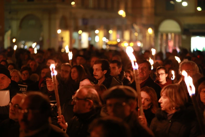 people holding up candles while a crowd stands in the background