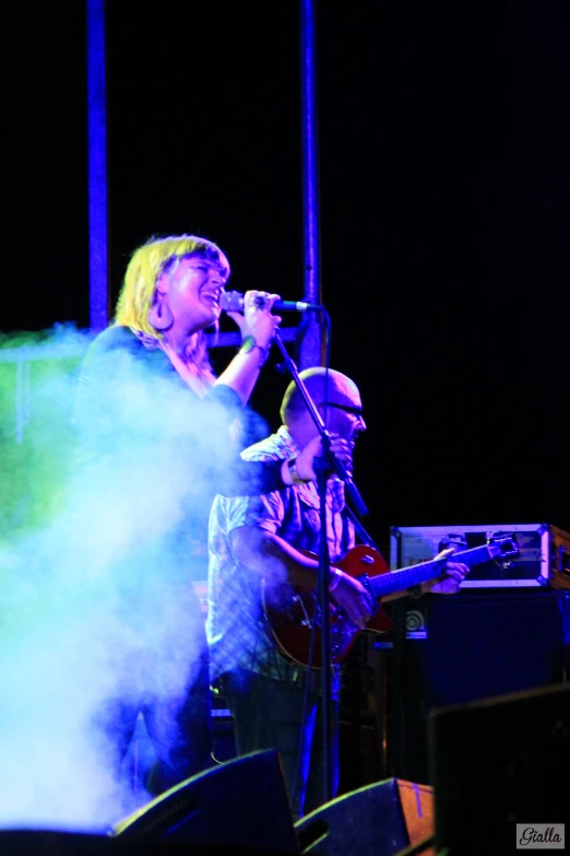 a woman singing into a microphone while holding a guitar