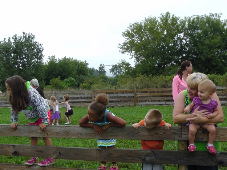 many children sit on a fence while others look over