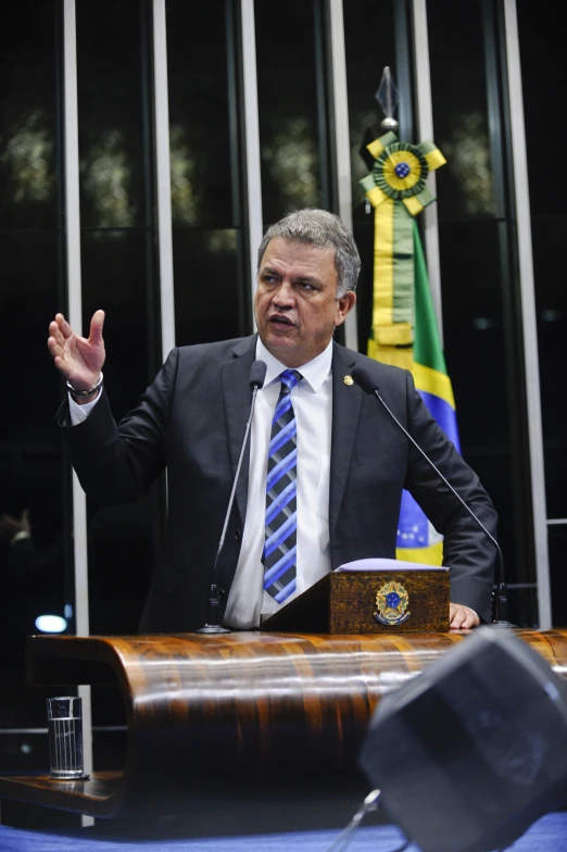 man speaking at podium with flag and two flags in background