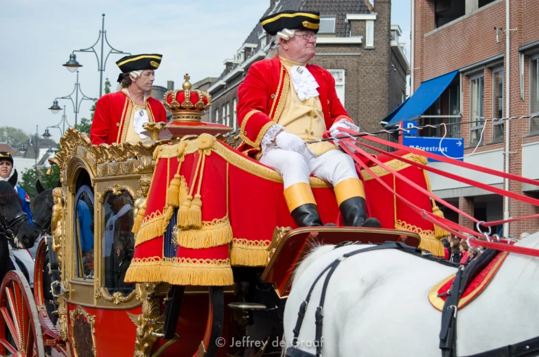 two men in red and gold uniforms riding a carriage