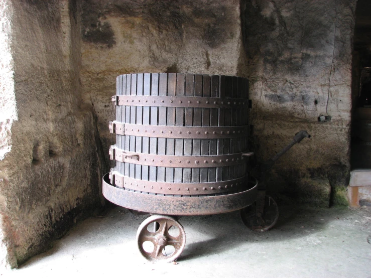 a large barrel sitting in a corner near a wheel