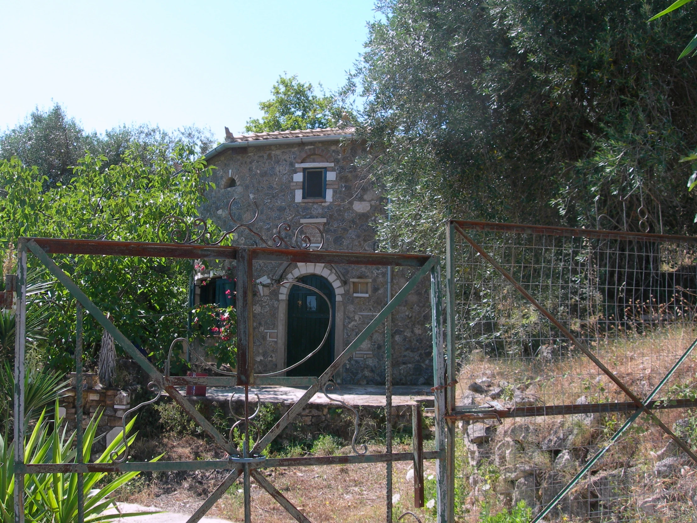 a gate leads to a small brick building surrounded by trees