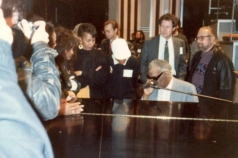 people gathered around a black piano while one man sings