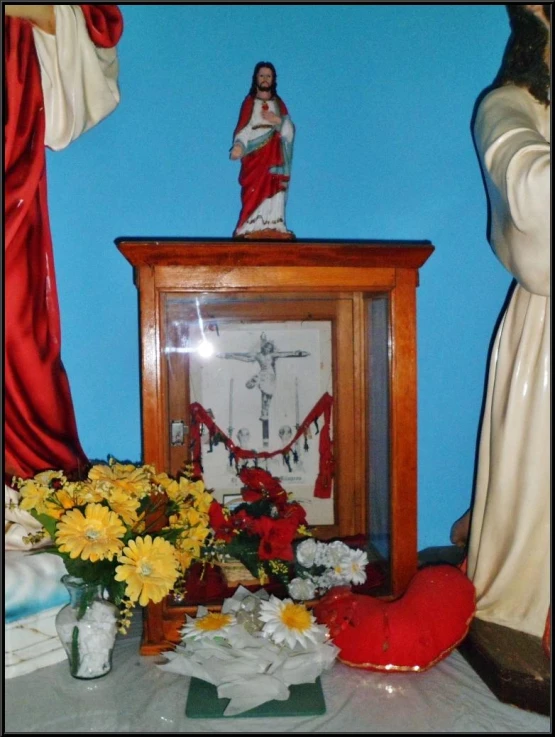 flowers and figurines are beside an old framed religious figure