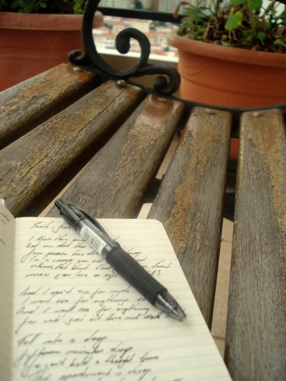 notepad with pen sitting on wooden bench next to potted plant
