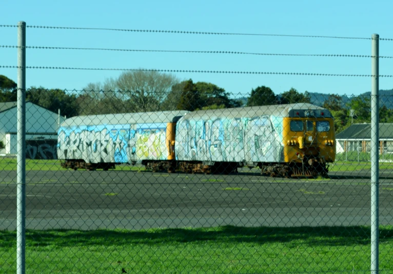 an old train with graffiti on the side and on it is near a chain link fence