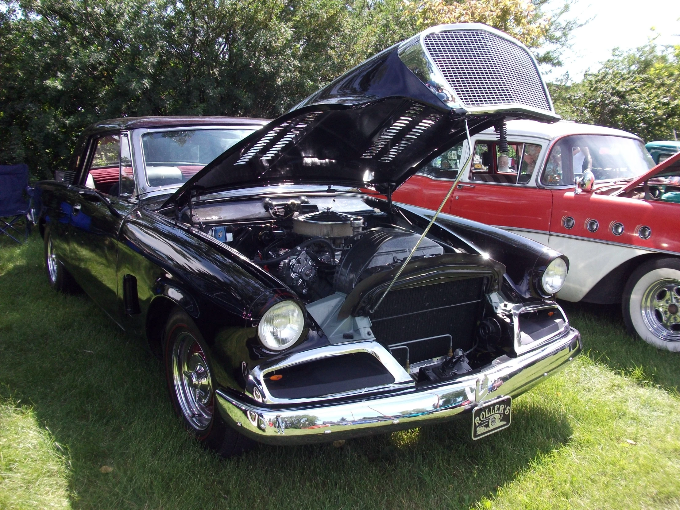 two vintage cars with hood up are sitting on the grass