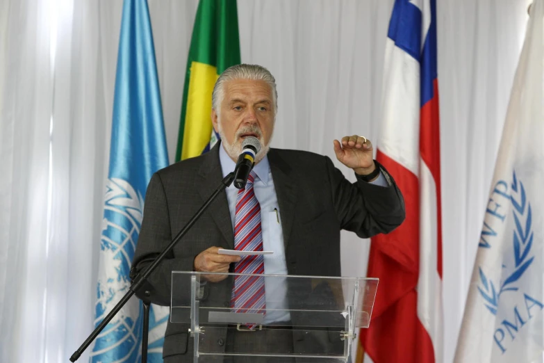 man in suit and tie holding microphone in front of flags