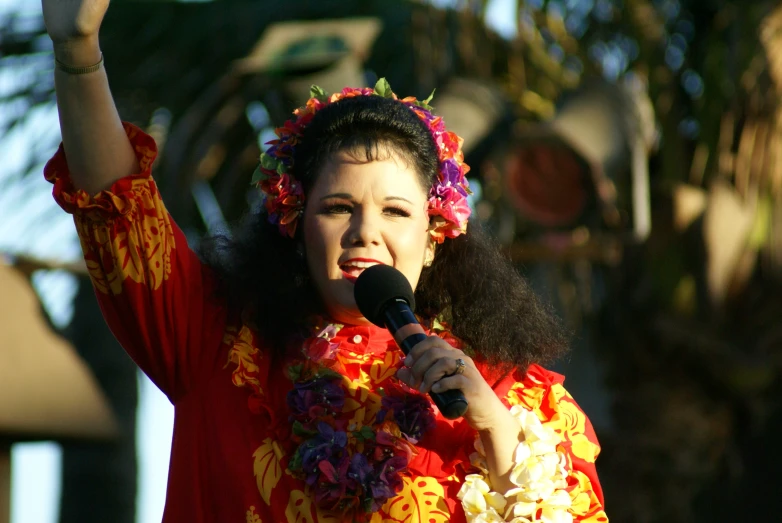 a woman wearing flowers holding her hands up in front of the microphone