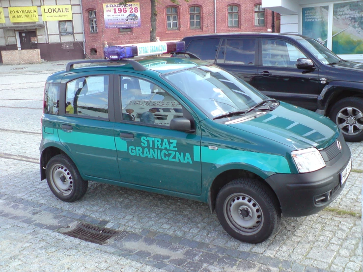 small green car parked on street next to another car