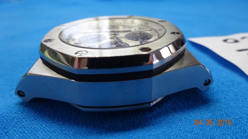 a metal watch on a blue cloth with a black rubber band